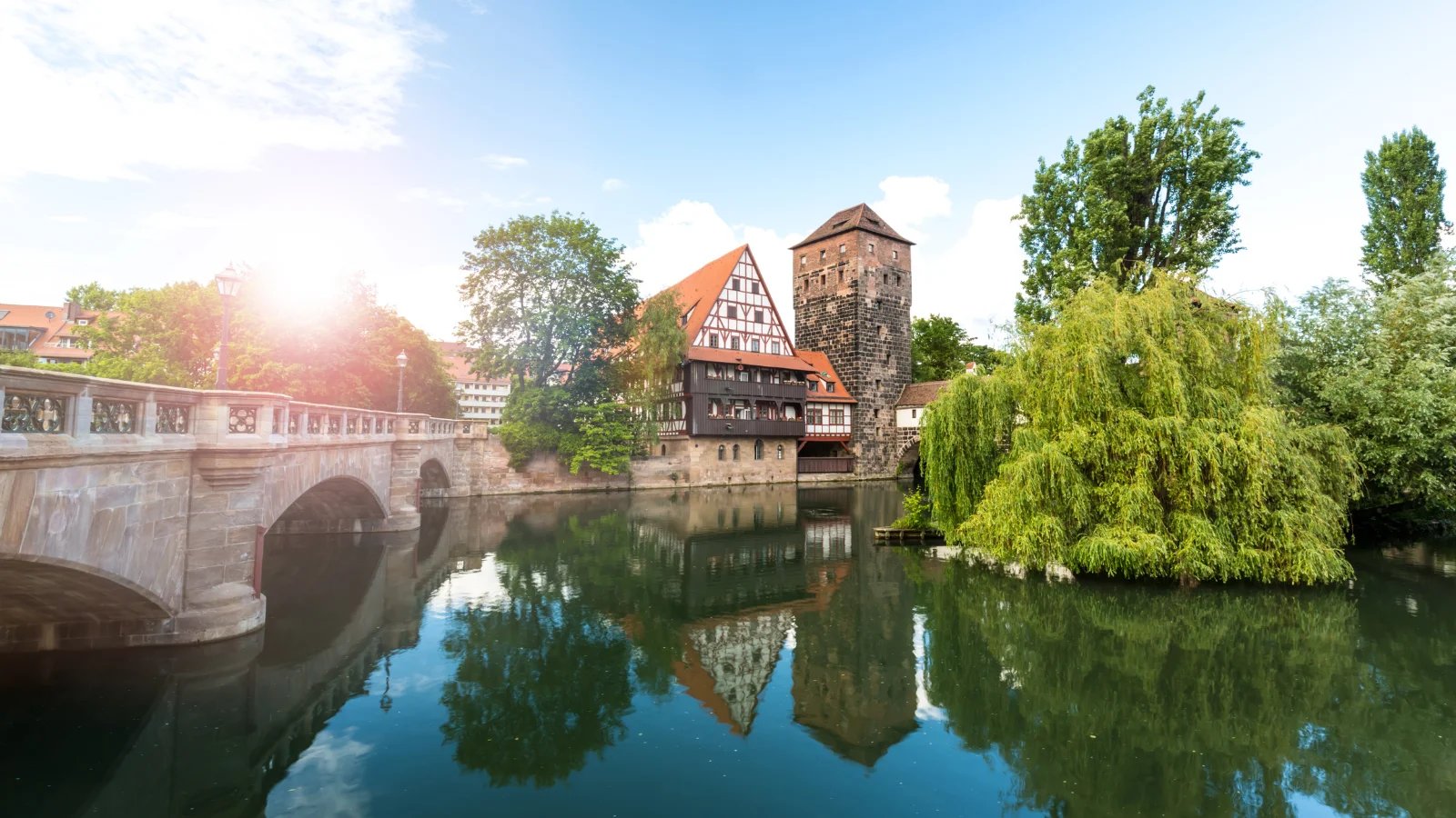vista panorámica de un puente de piedra, una casa de entramado y una torre de piedra a lo largo del río en el centro de Nuremberg, Alemania