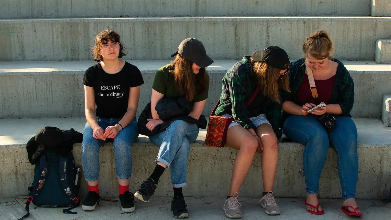 4 estudiantes de EDE sentados en un banco, 3 están mirando una foto en el teléfono de una chica